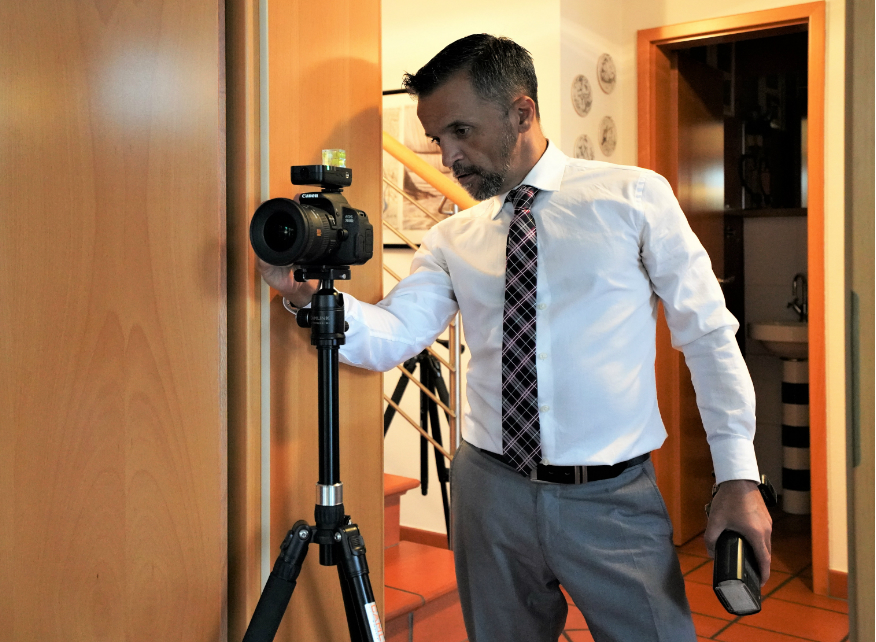 Smile! Young man focusing at you with digital camera while standing in studio with lighting equipment on background