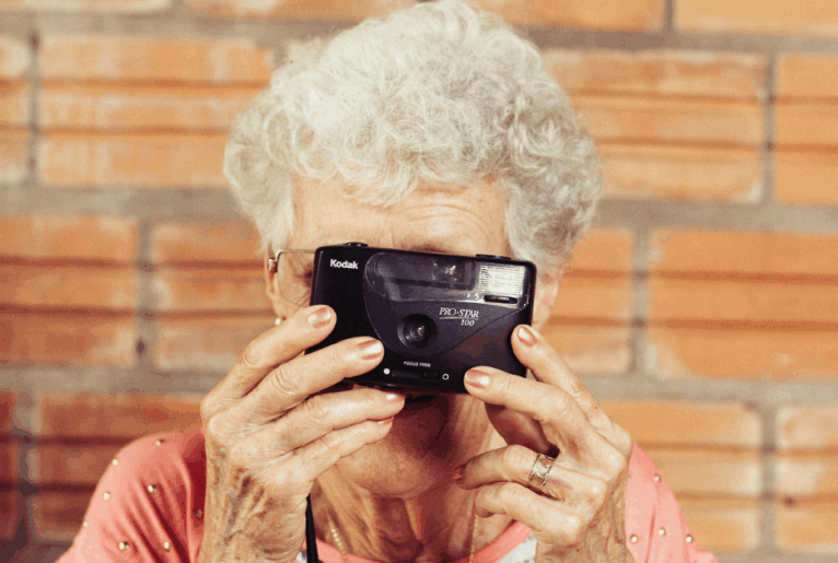 Immobilienverkauf im Pflegefall. Nahaufnahme einer älteren Dame mit Retrokamera vor dem Gesicht.